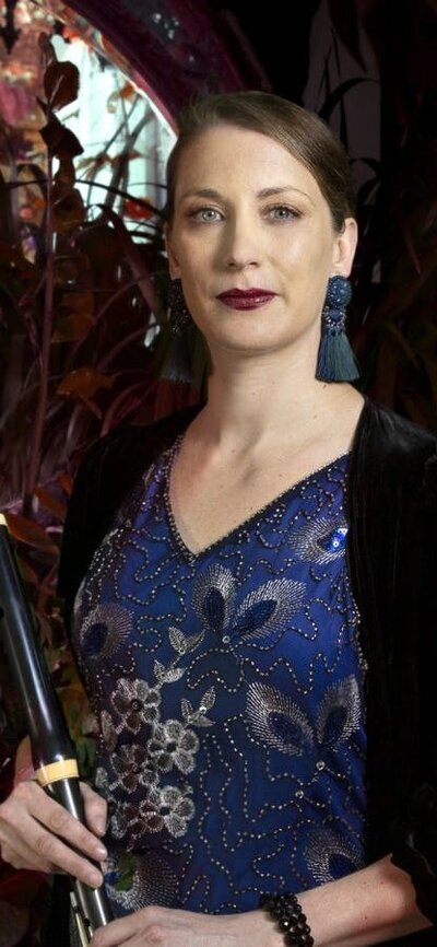Mikaela Oberg, performing withthe Australian Haydn Ensemble A flute plater in a blue dress against a background of lush leaves.