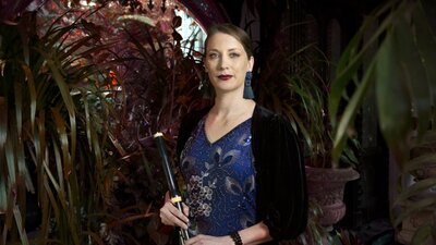 A flute plater in a blue dress against a background of lush leaves.