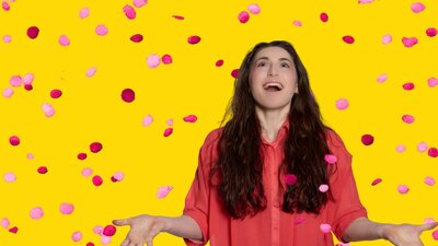 a young woman looks up with hand outstretched as pink rose petals fall on a yellow background
