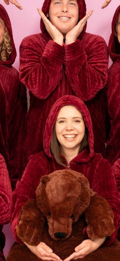 six people in plush red oodies smiling at the camera and making a heart shape by joining their hands