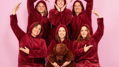 six people in plush red oodies smiling at the camera and making a heart shape by joining their hands
