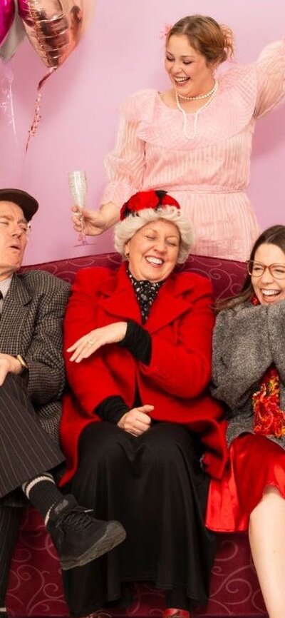 group of 6 people mixed ages sit on a red couch laughing