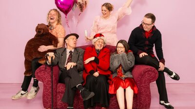 group of 6 people mixed ages sit on a red couch laughing