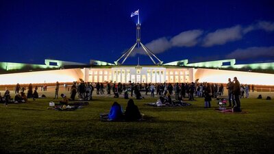 Night-time view of Australian Parliament House, brightly lit against a dark blue sky.