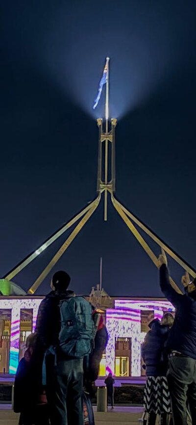 Night-time view of Australian Parliament House with the illuminated flag mast rising into a dark sky