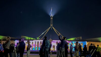 Night-time view of Australian Parliament House with the illuminated flag mast rising into a dark sky