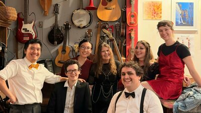 7 smiling improvisers in cabaret outfits in front of a wall of instruments