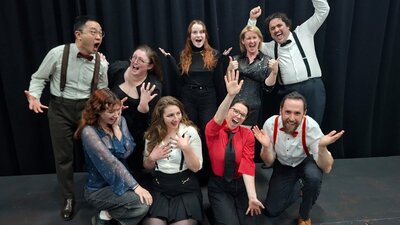 9 performers dressed up in cabaret outfits with fun lively expressions