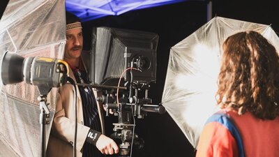 An image of a man setting up a large format camera, surrounded by studio lights