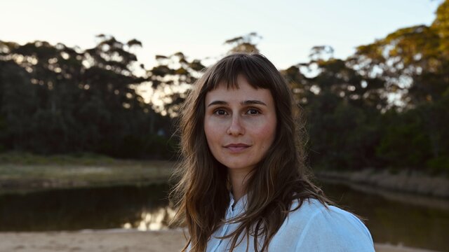Photo of the artist, Isabel Rumble Lady standing in front of a lake