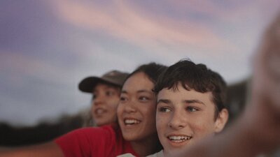 close up of 3 young people looking to the left of the frame. Sky is streaky with sunset colour