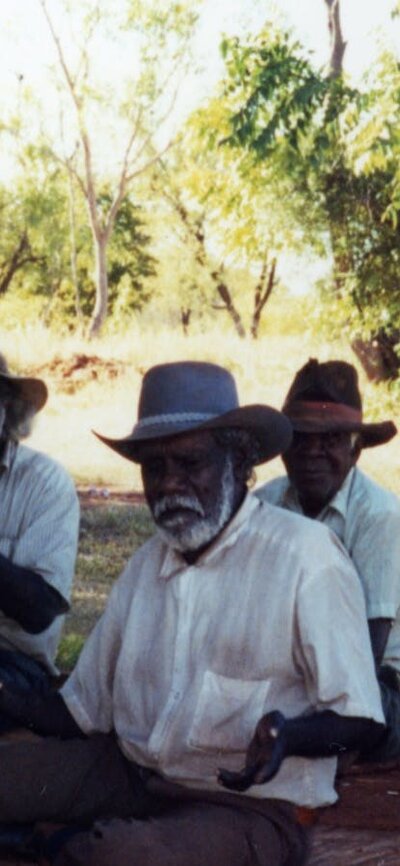 Asian man sitting on ground surrounded by Aboriginal men sitting with him in the desert