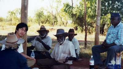 Asian man sitting on ground surrounded by Aboriginal men sitting with him in the desert