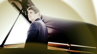Pianist Javier Perianes standing beside an open grand piano
