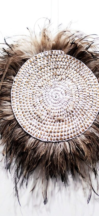 Circular woven wall hanging with feathers on a white wall