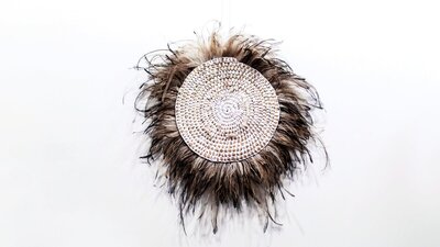 Circular woven wall hanging with feathers on a white wall