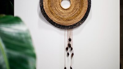 Circular woven wall hanging with a green plant in front on a white wall