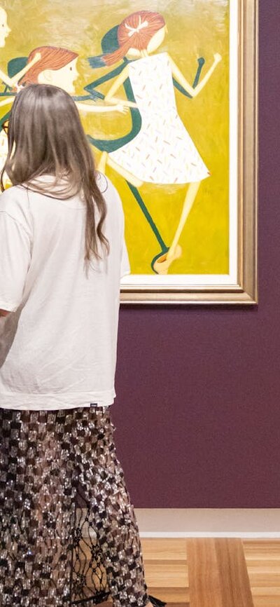 Two people in formal clothing view a portrait hung on a Gallery wall depicting three young girls.