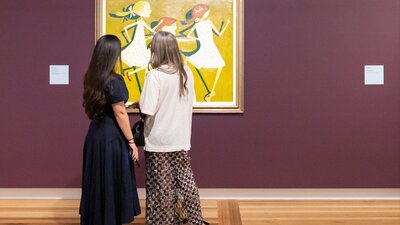 Two people in formal clothing view a portrait hung on a Gallery wall depicting three young girls.