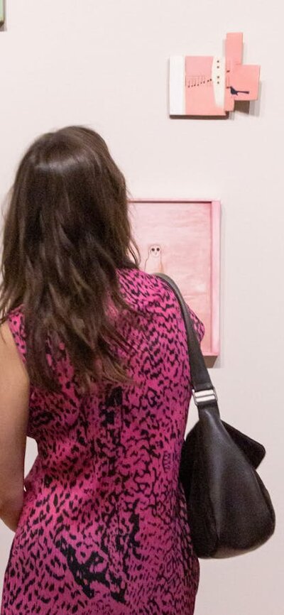A person wearing a patterned dress views several painted portraits on a light-coloured wall.