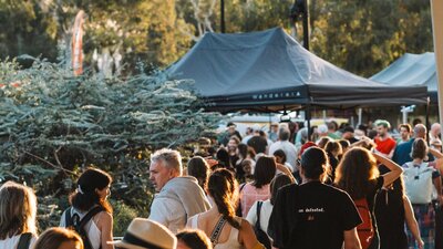 A bustling crowd outdoors at sunset. Tents and trees are visible,