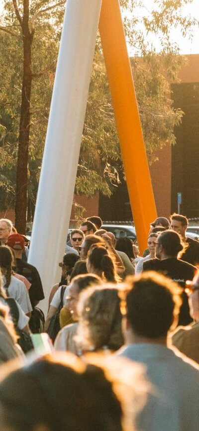 Bustling outdoor crowd at walking at sunset with marquees in the background.