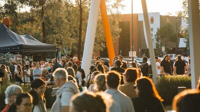 Bustling outdoor crowd at walking at sunset with marquees in the background.