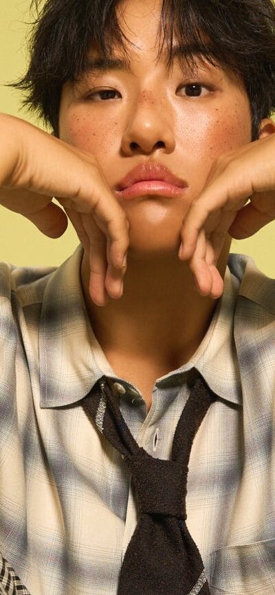 KINKY sitting down with his hands placed under his chin, with a yellow background