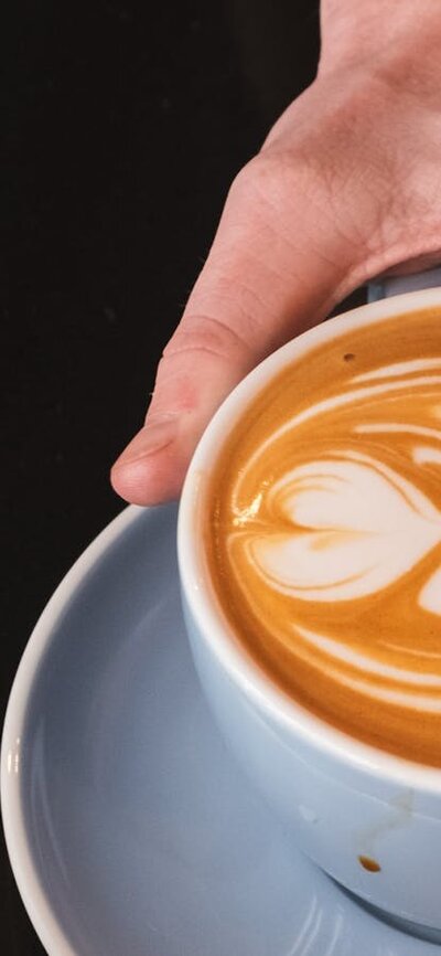 Closeup image of a cup of coffee being passed to a customer by CMAG barista
