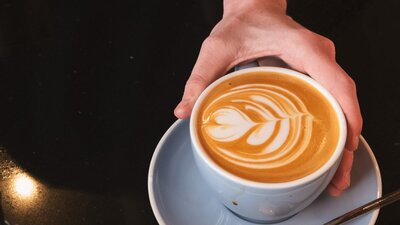 Closeup image of a cup of coffee being passed to a customer by CMAG barista
