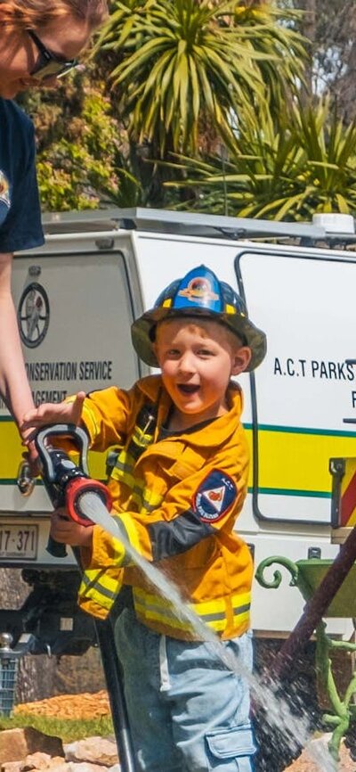 Kids Day Out A child using a firehose while supervised by a volunteer firefighter