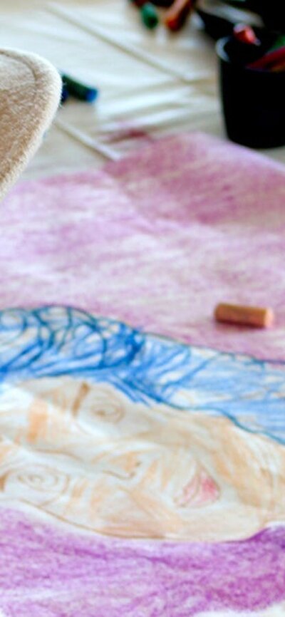 A young girl wears a felt hat, looking at a bright colourful artwork on her kite