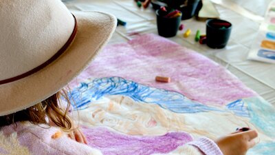 A young girl wears a felt hat, looking at a bright colourful artwork on her kite