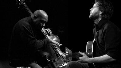 Black and white photo of person playing bass and person playing guitar