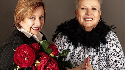 Divine Devilles Woman holding a bouchée of red flowers and another woman wearing a black feather scarf