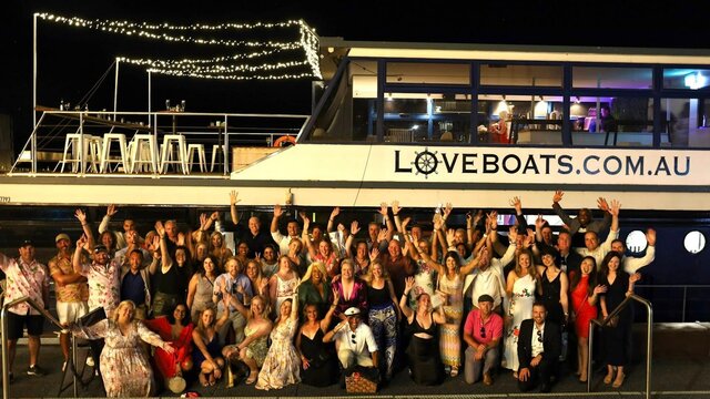 Large groups of cheering people standing next to a big boat called Love Boat Canberra