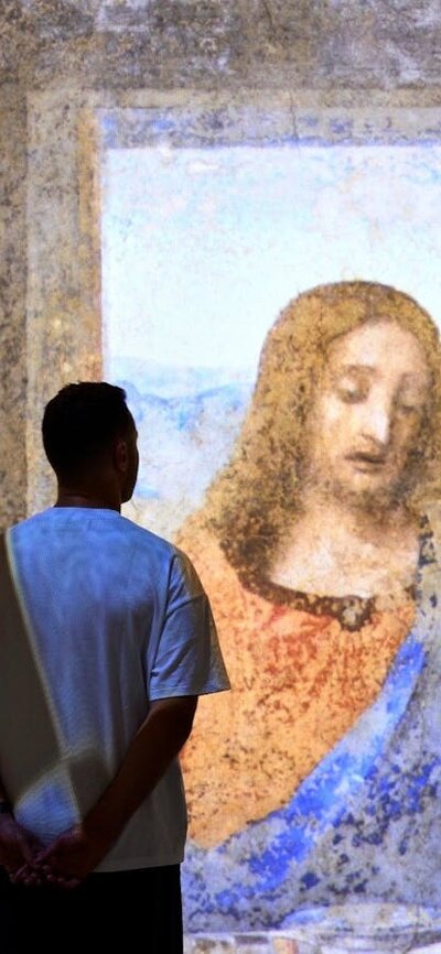 Visitors stand before a large immersive projection of The Last Supper in a gallery space.