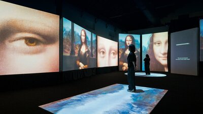 Visitors move through a digital gallery surrounded by immersive Mona Lisa projections.