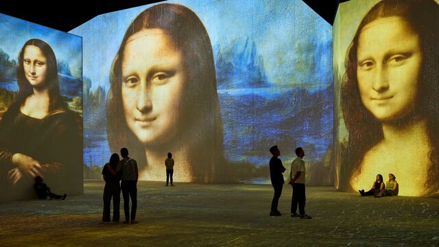 Stepping inside a masterpiece—Mona Lisa surrounds visitors in an immersive art experience. Visitors stand inside an immersive gallery as Mona Lisa projections glow across towering walls.