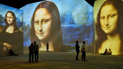 Stepping inside a masterpiece—Mona Lisa surrounds visitors in an immersive art experience. Visitors stand inside an immersive gallery as Mona Lisa projections glow across towering walls.