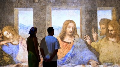 A timeless moment, reimagined—The Last Supper experienced at immersive scale. Visitors stand before a large immersive projection of The Last Supper in a gallery space.