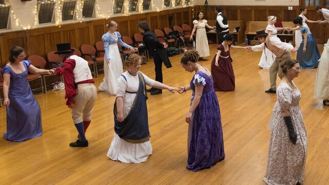 A group of dancers in a ballroom bowing to each other, dressed in Regency outfits.