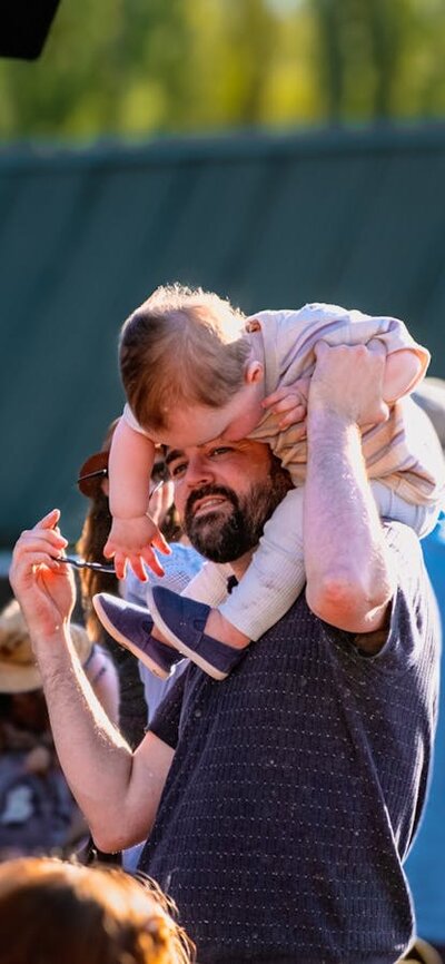 Parent lifting small child on his shoulders to dance and enjoy Live at Lanyon