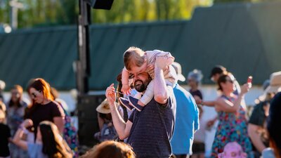 Parent lifting small child on his shoulders to dance and enjoy Live at Lanyon