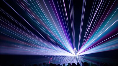 Still from Triptych by Robin Fox showing vivid purple laser projection in a dark room with audience