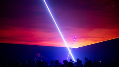 Still from Triptych by Robin Fox showing a laser projection in a dark room with audience in shadow