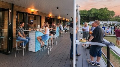 People sitting and standing along an outdoor deck next to a bowling green