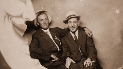 Archival image of two men sitting on a sign of a crescent moon looking at camera