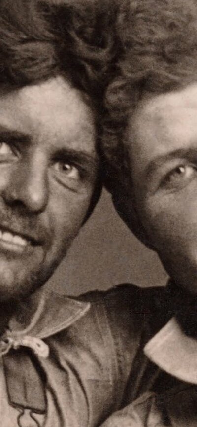 An archival photograph of two working men with an arm around the neck of the other