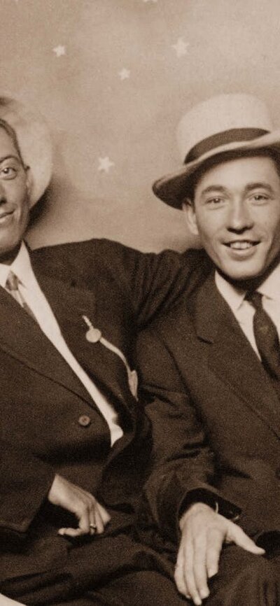 Archival image of two men sitting on a sign of a crescent moon looking at camera